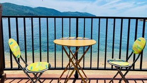 A balcony with two yellow chairs and a small round table, overlooking a calm sea and distant mountains.