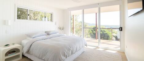 A bedroom with a bed, a nightstand, a window, and a sliding glass door leading to a balcony.
