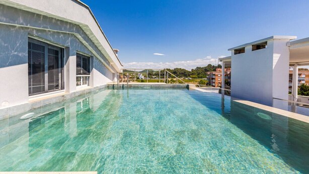 Una piscina al terrat amb aigua cristal·lina, envoltada d'edificis moderns i un cel serè.