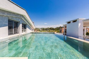 Une piscine sur le toit, avec une eau cristalline, entourée de bâtiments modernes et sous un ciel dégagé.