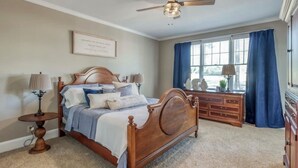 Een slaapkamer met een houten bed, nachtkastje, dressoir en plafondventilator.