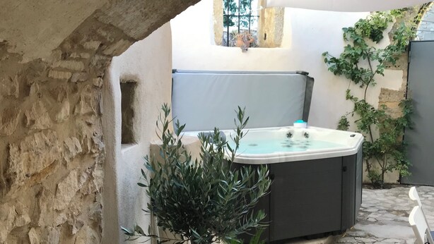 Een stenen binnenplaats met een hottub, potplanten en een uitzicht op een gebouw door een boog.
