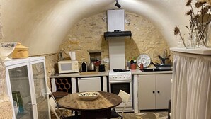 Een rustieke keuken met stenen muren, een houten tafel en een wit kastje.