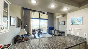 A kitchen with granite countertops, a dining area with a table and chairs, a ceiling fan, and a view of the ocean through large windows. -  2-bedroom apartment with WiFi, AC in Kihei (Kihei)