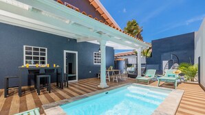 A pool area with a tiled deck, a covered seating area, and a pool. - Casa Sol • Stylish 4 BR Villa with Private Pool (Noord)