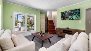 A living room with a sofa set, a coffee table, a TV mounted on the wall, and a staircase leading to another level. - Casa Sol • Stylish 4 BR Villa with Private Pool (Noord)