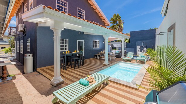 A pool area with a covered patio, lounge chairs, and a dining setup. - Casa Sol • Stylish 4 BR Villa with Private Pool (Noord)
