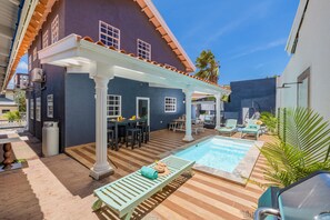 A pool area with a covered patio, lounge chairs, and a dining setup. - Casa Sol • Stylish 4 BR Villa with Private Pool (Noord)