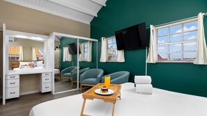 A hotel room with a bed, a bedside table with a tray of breakfast, a mirror, a TV, and a window with curtains. - Casa Sol • Stylish 4 BR Villa with Private Pool (Noord)