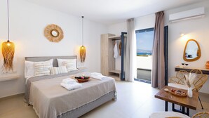 A modern bedroom with a large bed, bedside tables, a dining area with wicker chairs, and a view of the sea through the window. - Cezaria Naxos Hotel (Naxos)
