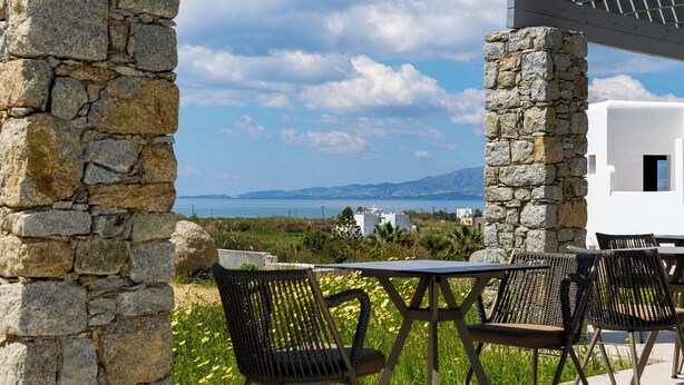 A stone structure with a pergola overhead, outdoor seating, and a view of the sea and mountains. - Cezaria Naxos Hotel (Naxos)
