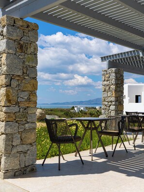 A stone structure with a pergola overhead, outdoor seating, and a view of the sea and mountains. - Cezaria Naxos Hotel (Naxos)