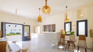 A modern hotel lobby with a marble floor, a reception desk, wicker furniture, and hanging pendant lights. - Cezaria Naxos Hotel (Naxos)