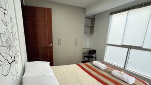 Una habitación de hotel moderna con una cama grande, un armario, un escritorio y una ventana con persianas.