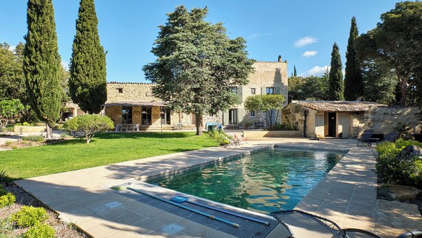 A pool area with a stone building, a grassy lawn, and tall trees. - My family home (Vers-Pont-du-Gard)