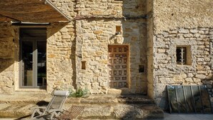 A stone building with a wooden door, a metal bench, and a glass door. - My family home (Vers-Pont-du-Gard)