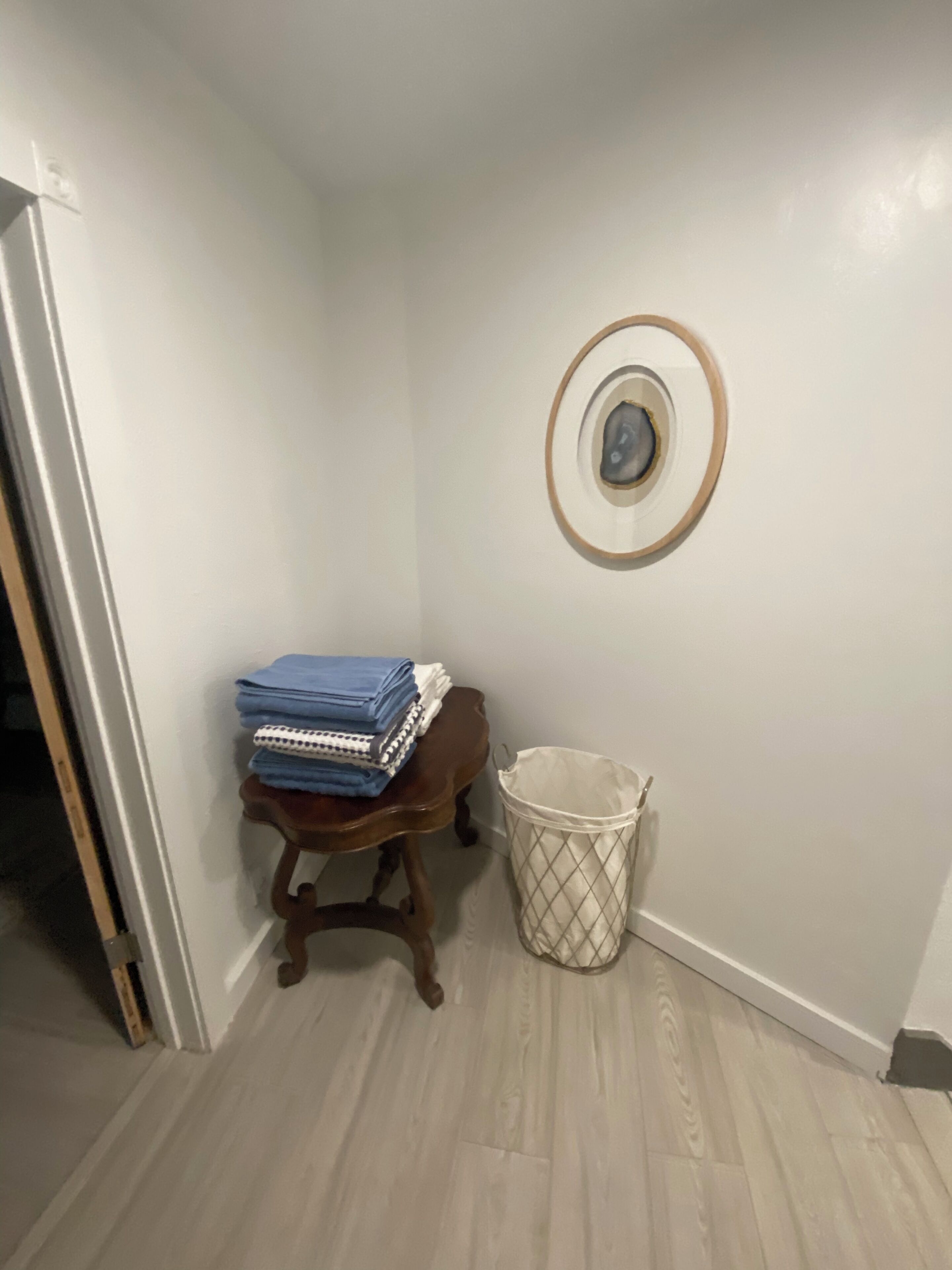 A corner of a room with a wooden chair, a trash bin, and a wall-mounted circular object.
