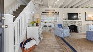 A spacious living area with a staircase, a fireplace, a television, and a dining area. - Scituate Seaside Escape – Sleeps 8, Walk to Beach (Scituate)