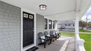 A porch with three Adirondack chairs, a black door, and a white railing. - Scituate Seaside Escape – Sleeps 8, Walk to Beach (Scituate)