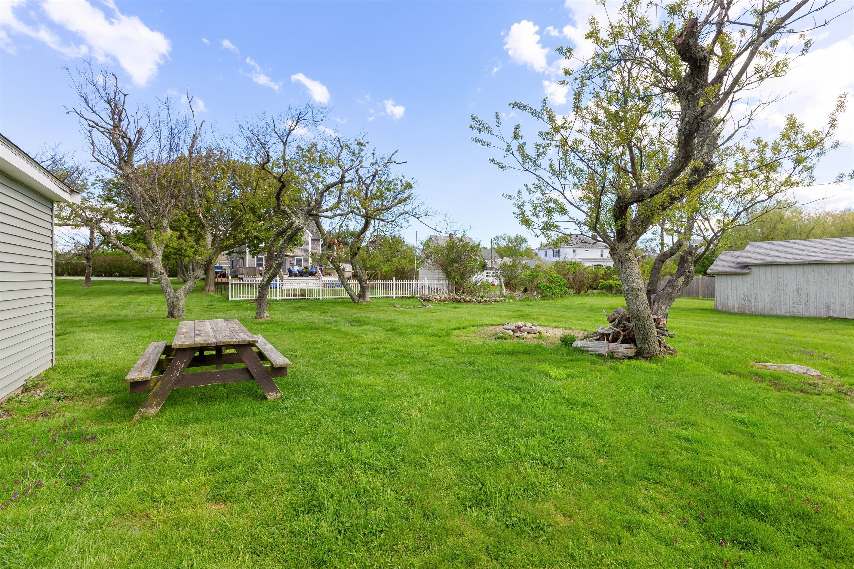 Un patio trasero con una mesa de picnic, un cobertizo y una valla blanca.