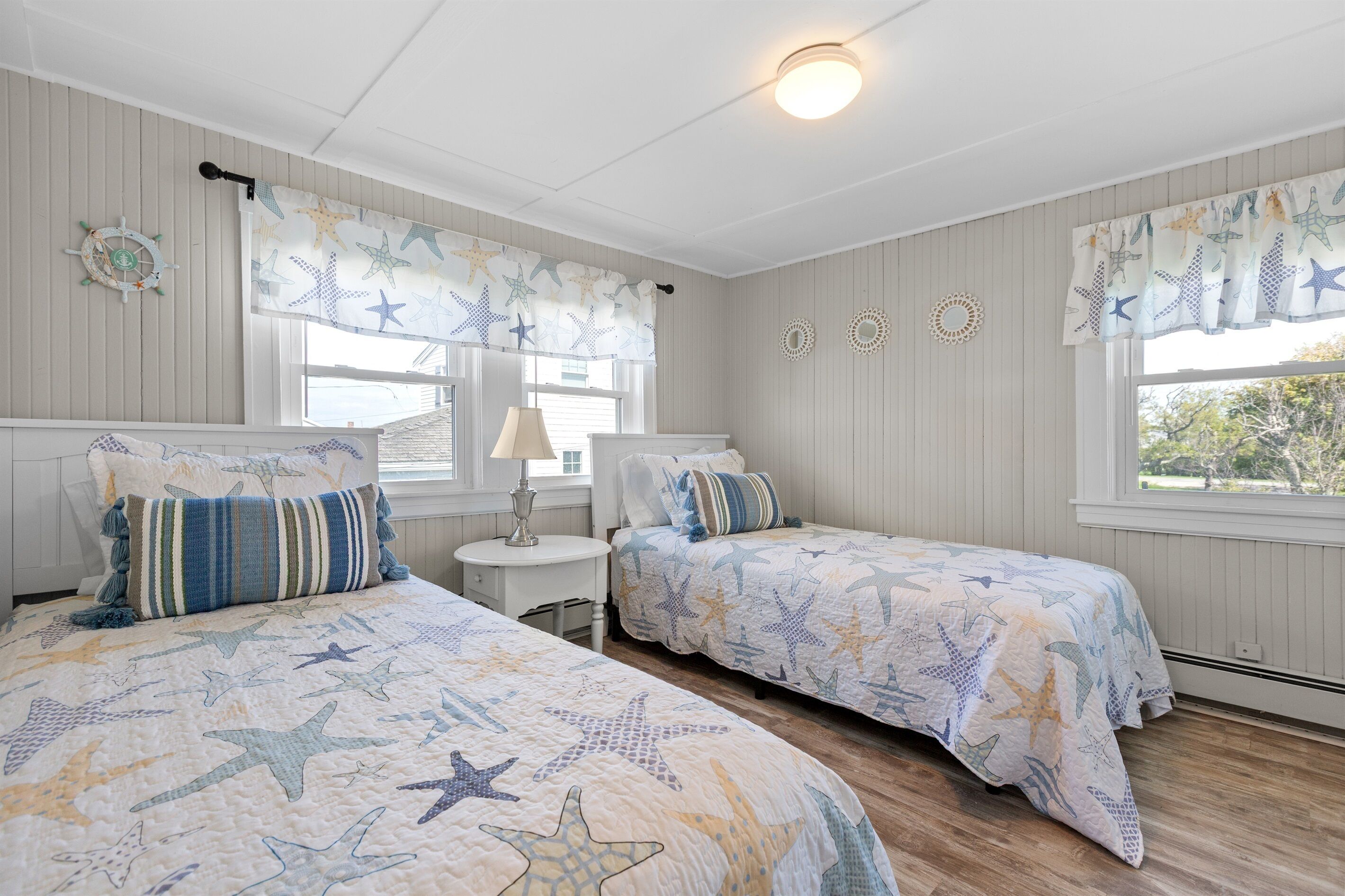 Une chambre avec deux lits, chacun agrémenté de draps à motifs d’étoiles, une petite table avec une lampe et une fenêtre ornée de rideaux sur le thème des étoiles.