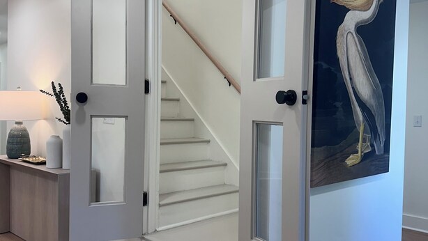 A modern interior with a staircase, a door with glass panels, and a wall-mounted painting of a pelican. - NEW 30+ day Modern Coastal 4bdrm 2 Masters (Mount Pleasant)