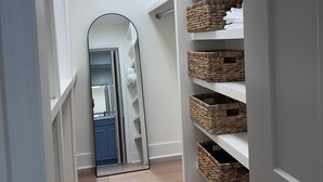 A narrow hallway with white shelving units and wicker baskets, leading to a mirrored closet door. - NEW 30+ day Modern Coastal 4bdrm 2 Masters (Mount Pleasant)