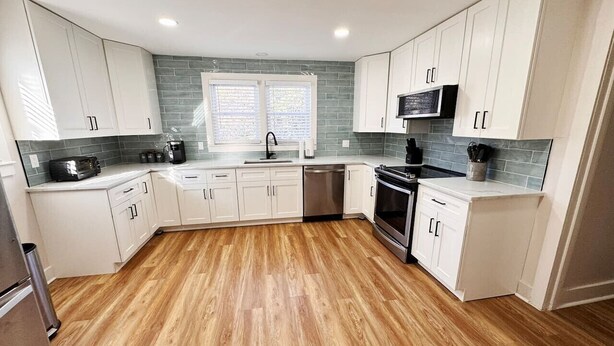 A modern kitchen with white cabinets, a stainless steel refrigerator, a dishwasher, and a microwave. - Charming Central Home-3bd/1bath (Danville)