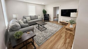 A modern living room with a grey sofa, a coffee table, a TV, and a wooden side table. - Charming Central Home-3bd/1bath (Danville)