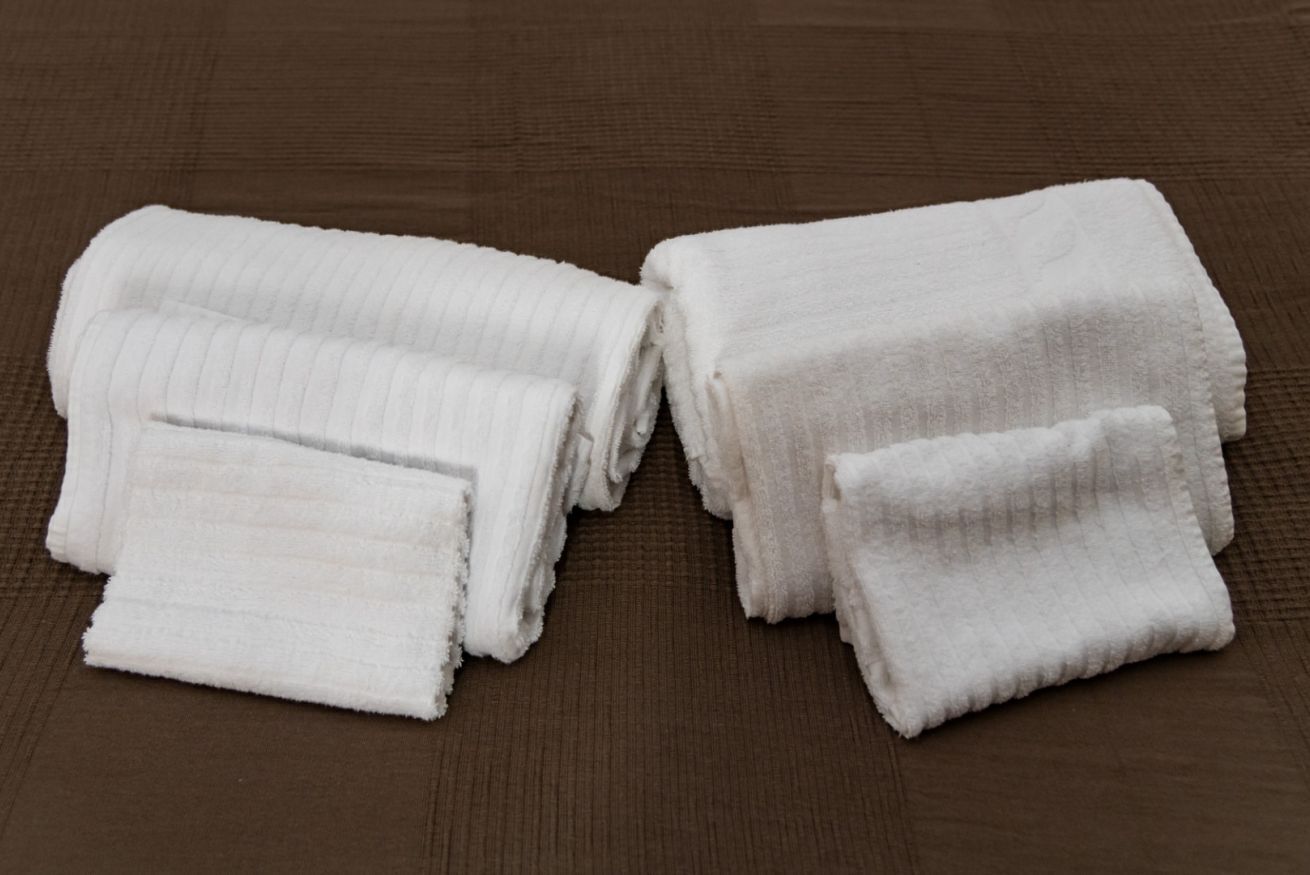 A set of neatly folded white towels on a textured brown surface.