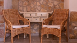 Deux fauteuils en osier avec des coussins blancs, un mur en pierre et une commode blanche à tiroirs.