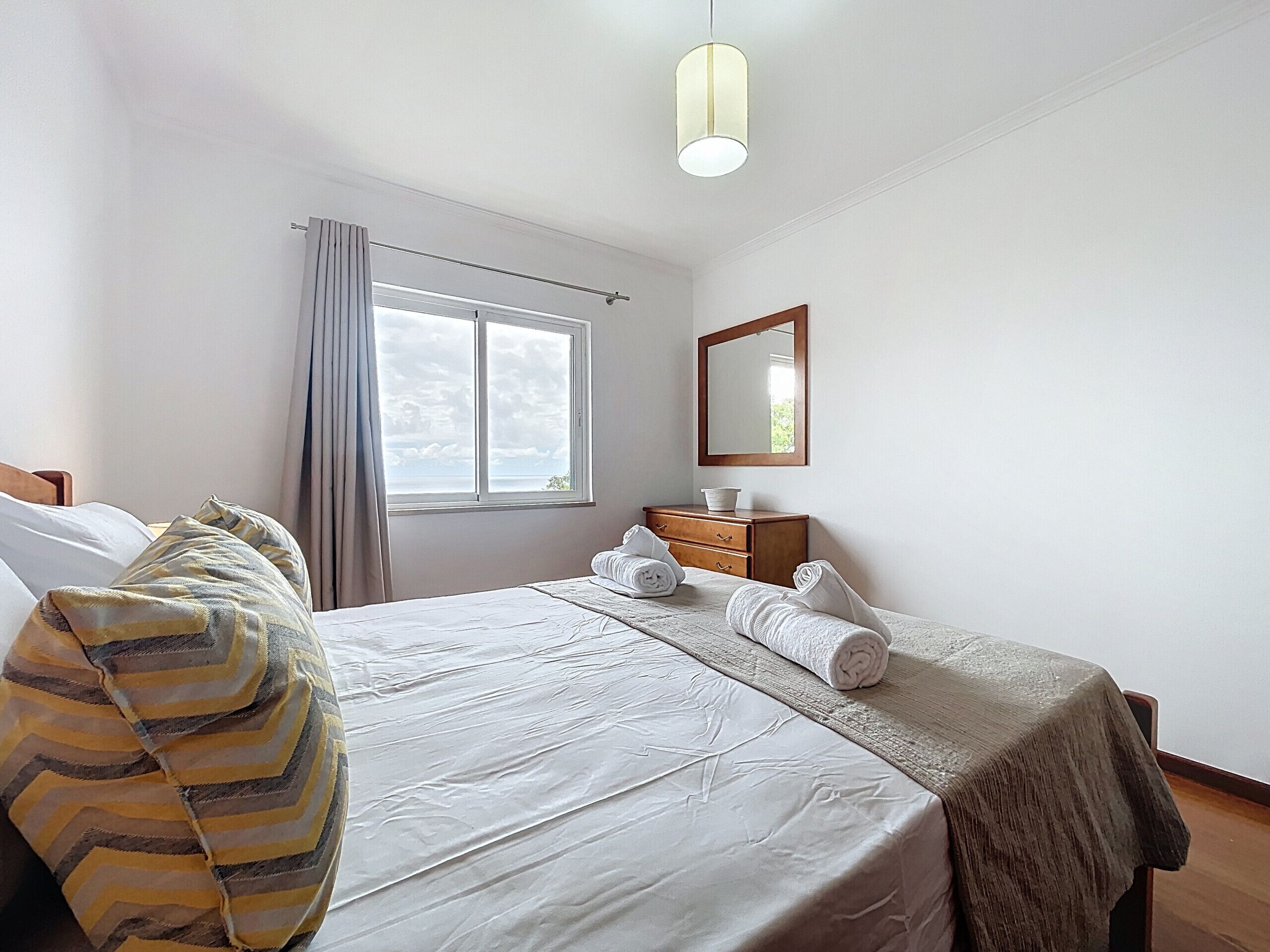 A neatly arranged hotel room with a large bed, a bedside table, a mirror, and a window with curtains.