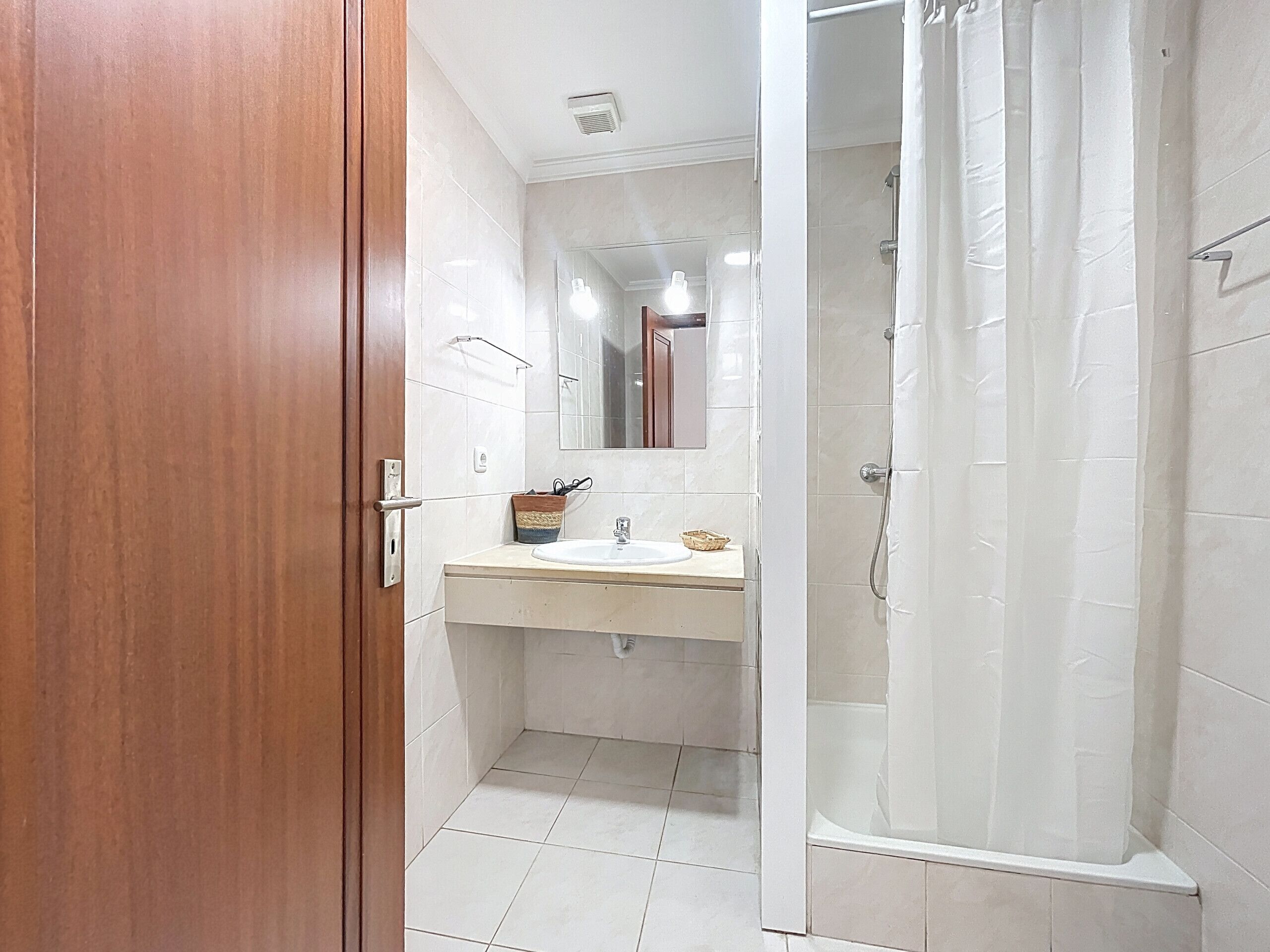 Un baño con puerta de madera, lavabo, espejo y zona de ducha.