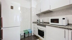 Une cuisine compacte avec des meubles blancs, un four à micro-ondes, une machine à café et un réfrigérateur.