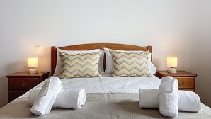 Un lit bien fait, avec deux oreillers, deux lampes de chevet et deux serviettes enroulées posées sur une couvre-lit à motifs.