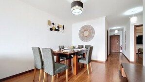 Un coin repas avec une table en bois et des chaises à revêtement gris, un élément décoratif mural et un couloir menant à une porte.