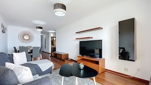 Un salon moderne avec un canapé, un téléviseur et un coin repas à l’arrière-plan.