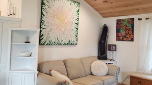 Ett mysigt vardagsrum med en beige soffa, ett vitt skåp, en takfläkt och en stor tavla med blommotiv.