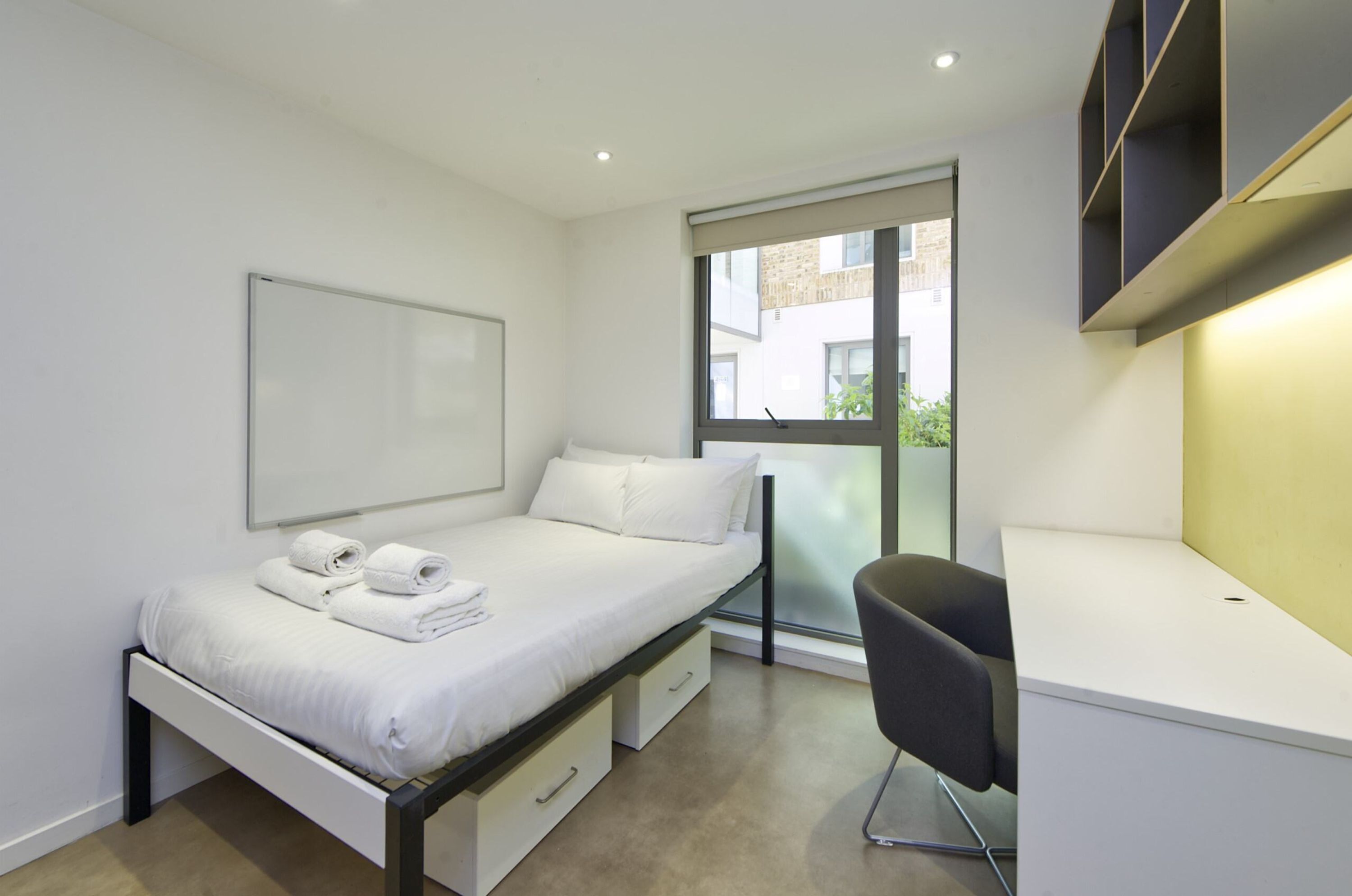 A modern bedroom with a bed, a desk, and a window.