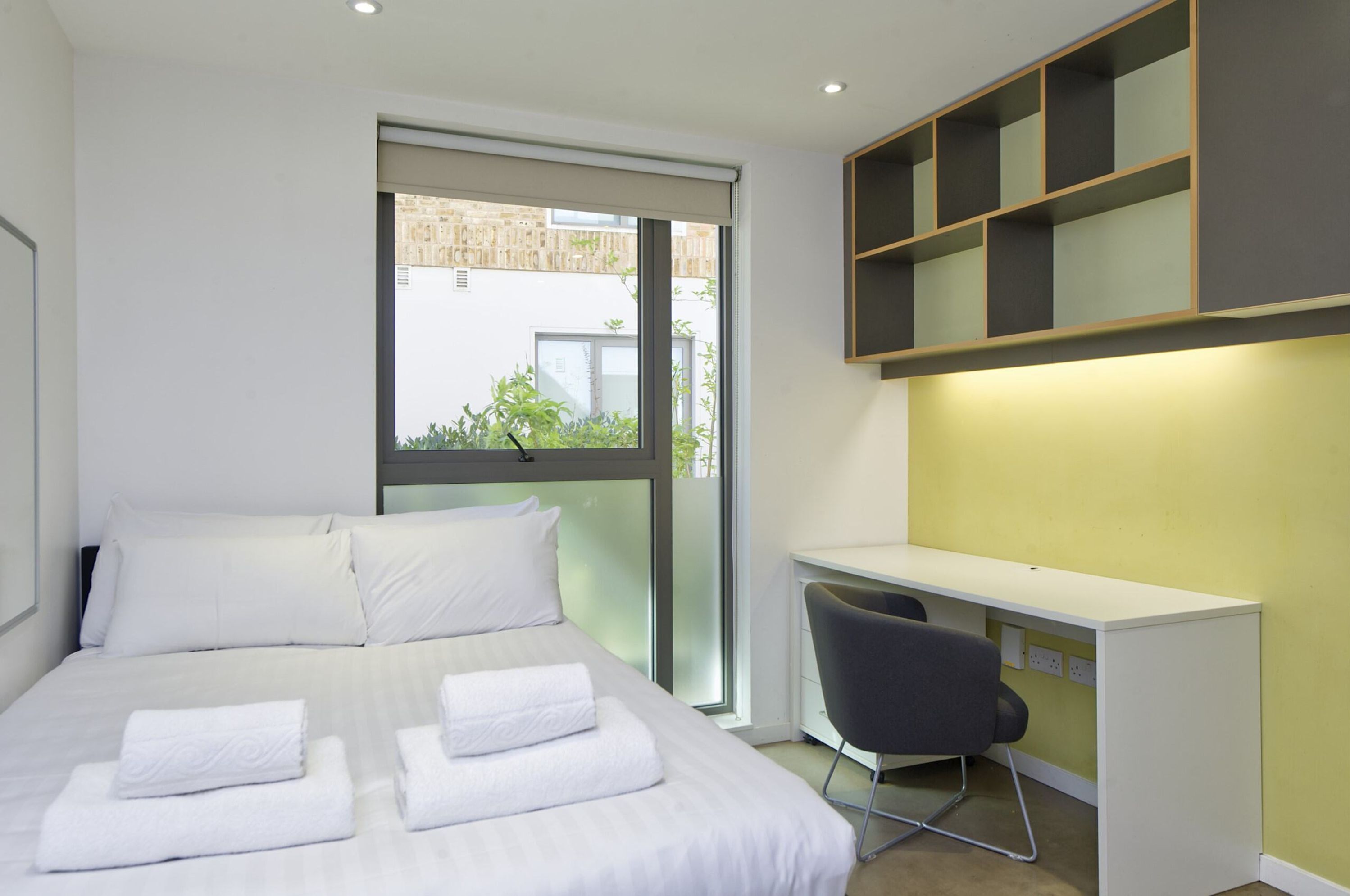 A modern hotel room with a large bed, a desk, and a chair.