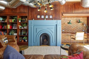 A cozy living room with a blue fireplace, leather sofas, a bookshelf, and a brick wall. - Modern-style Student Studio in London (London)
