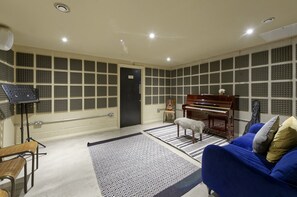 A recording studio with soundproofing panels, a grand piano, a mixing console, and a cozy blue sofa. - Modern-style Student Studio in London (London)