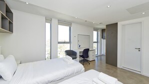 A modern hotel room with two beds, a desk, and a large window offering a city view. - Modern-style Student Studio in London (London)