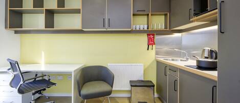A modern kitchen with grey cabinets, a white countertop, a black chair, and a small trash bin.