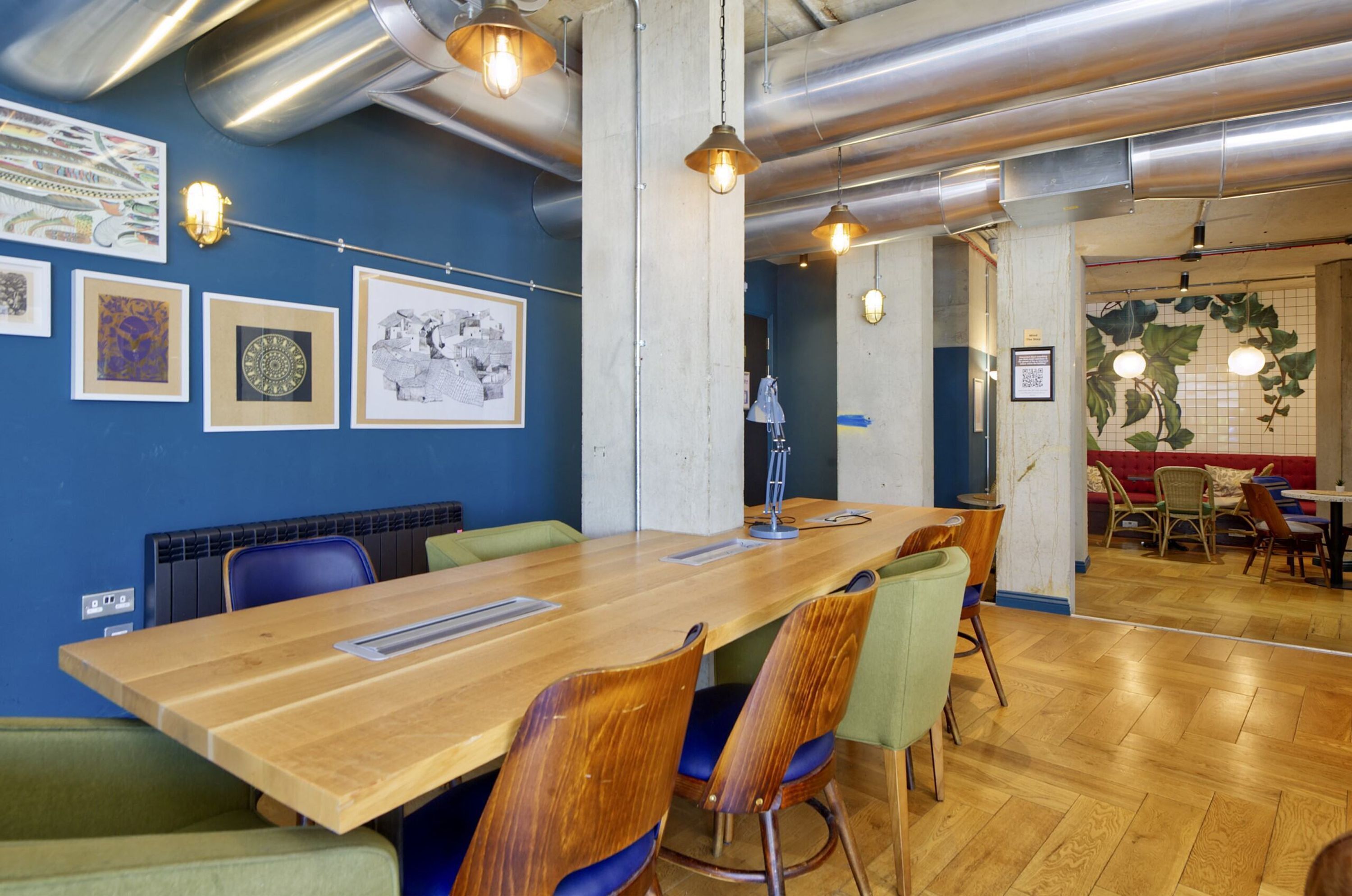 Een vergaderruimte met een lange houten tafel, groene en blauwe stoelen, en kunstwerken aan de wanden.