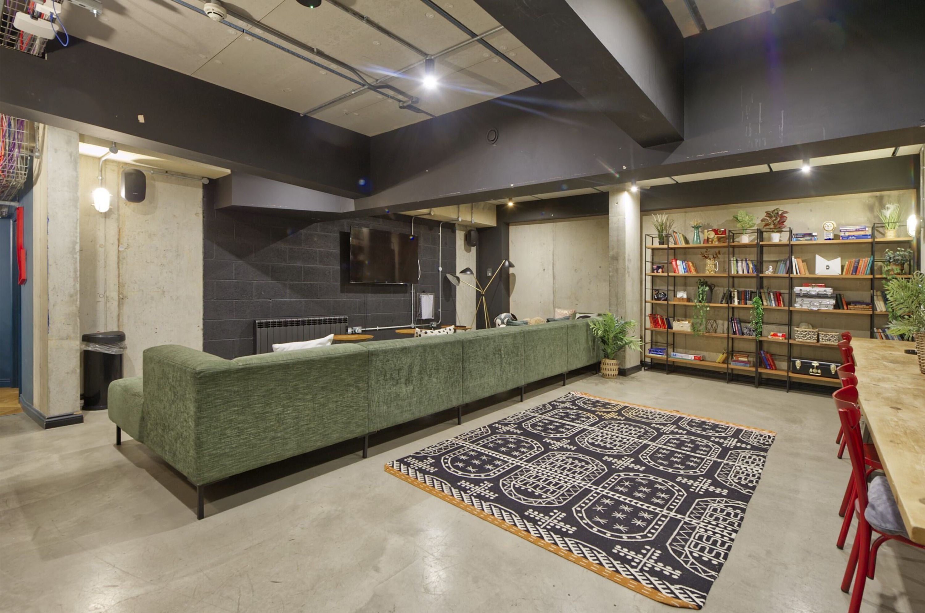 A modern lounge area with a green sofa, a patterned rug, a bookshelf, and a fireplace.