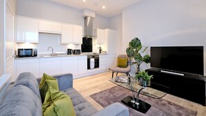 A modern living room with a grey sofa, a glass coffee table, and a flat-screen TV. - Modern City Centre Apartment in Aberdeen (Aberdeen)