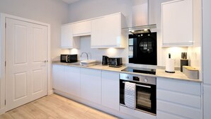 A modern kitchen with white cabinetry, a built-in oven, and a microwave. - Modern City Centre Apartment in Aberdeen (Aberdeen)