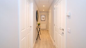 A narrow hallway with white doors, a small table with a plant, and a framed picture on the wall. - Modern City Centre Apartment in Aberdeen (Aberdeen)