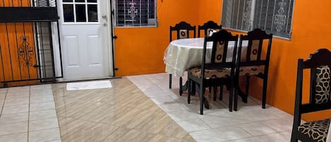 A dining area with a table and chairs, a door, and windows with metal bars.